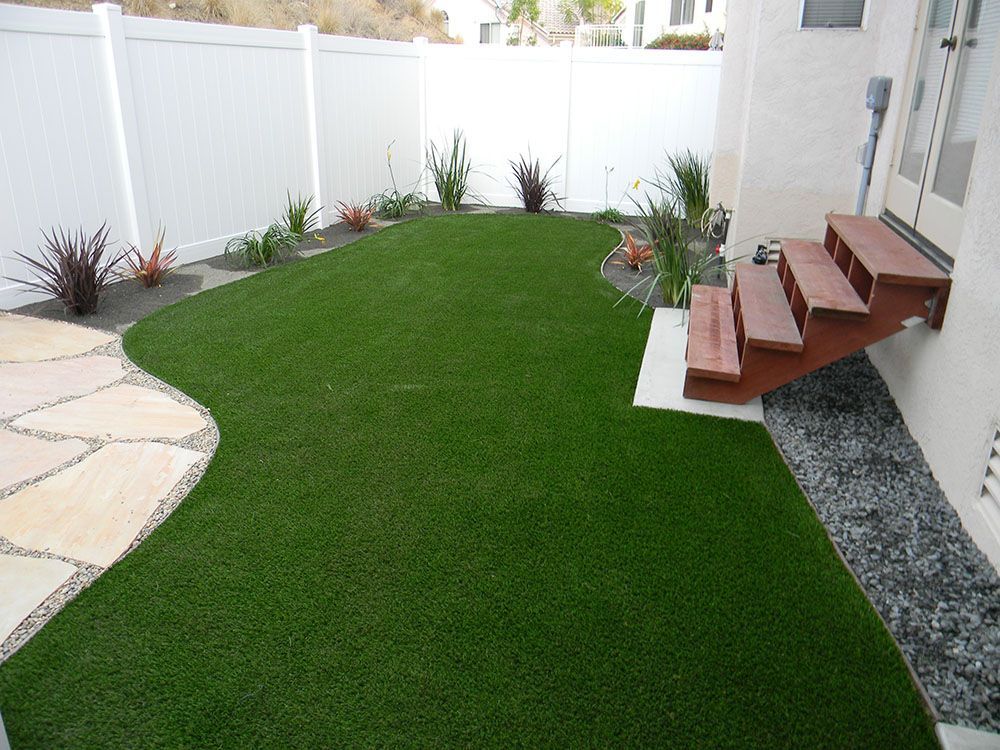 Backyard with green artificial turf, white fence, stone path, and wooden steps by the house
