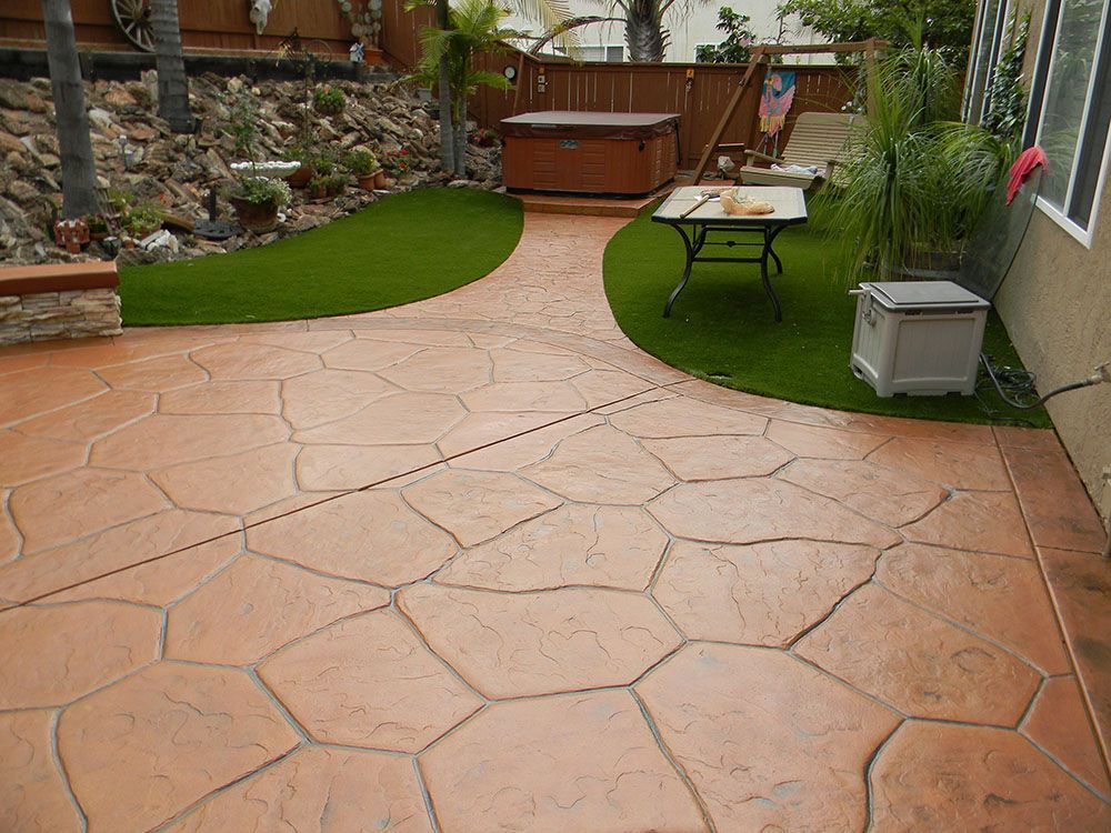 Backyard patio with stamped concrete, small lawn patch, potted plants, table, and hot tub