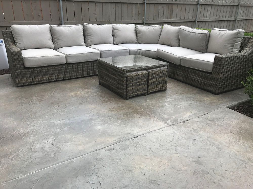 L-shaped gray outdoor sectional with white cushions and woven coffee table on a concrete patio