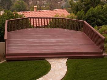 Large wooden deck with railings in a backyard, leading to a stone path and lawn.