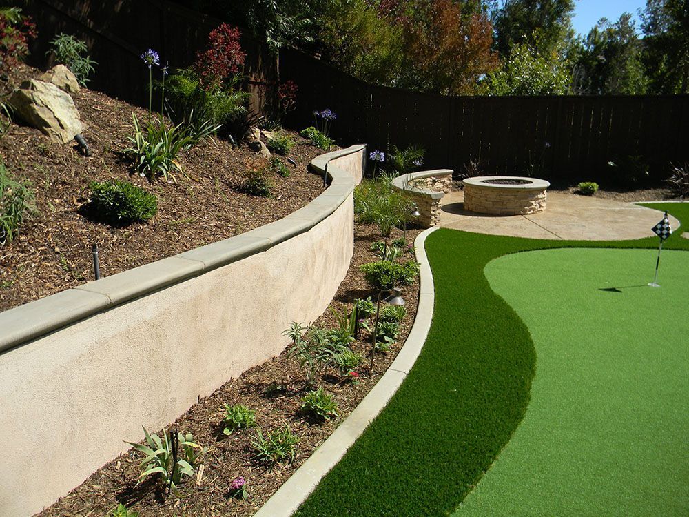 Landscaped backyard with curved retaining wall, green turf, and a circular fire pit area.