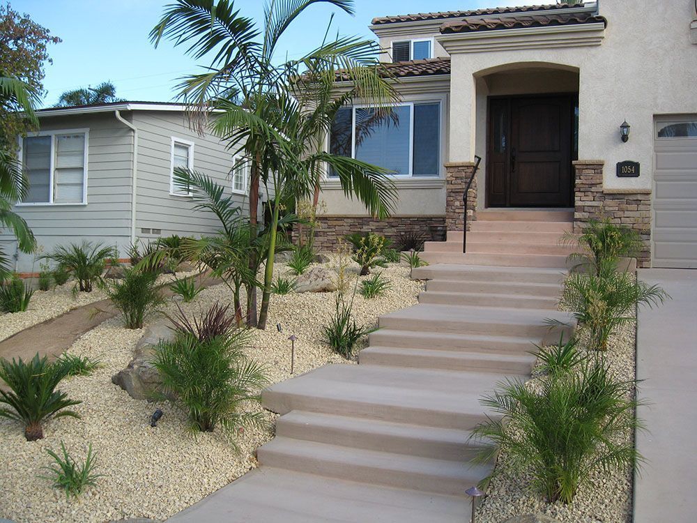 Modern house entrance with wide steps, desert landscaping, and palm trees under a blue sky