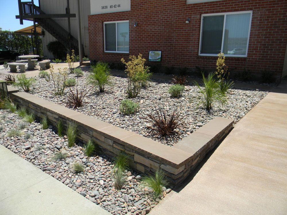Landscaped courtyard with gravel beds, small shrubs, and concrete walkways beside a brick building
