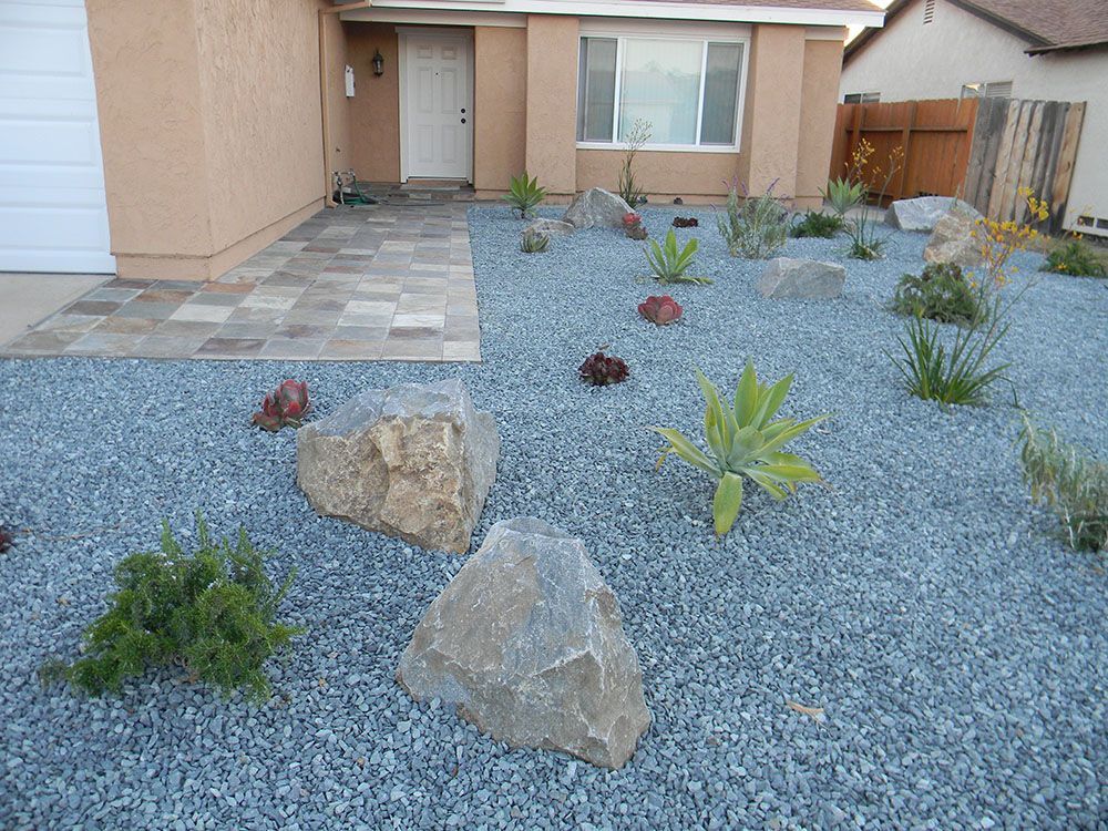 Front yard with blue gravel, large rocks, and sparse desert plants beside a house entryway