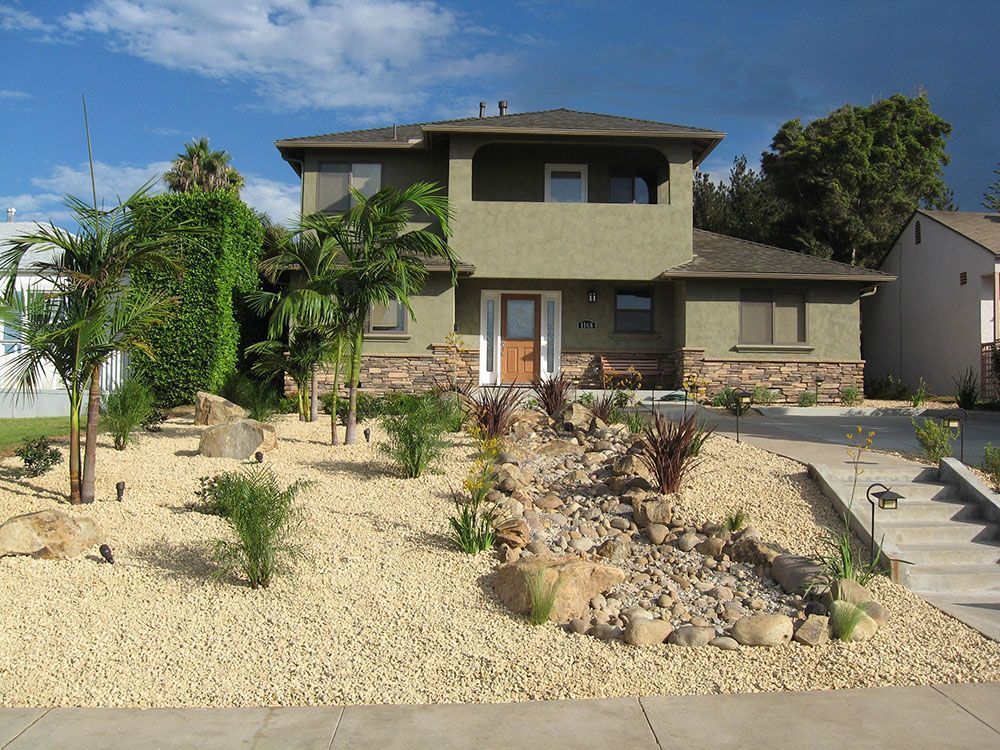 Two-story house with desert landscaping and a stone walkway under a blue sky.