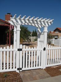 White picket gate and pergola entrance in a front yard under a clear blue sky
