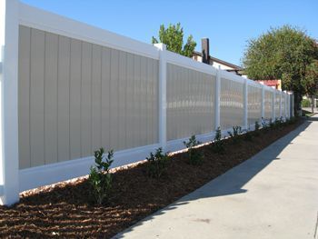 White privacy fence beside a sidewalk with trees and shrubs along a residential street