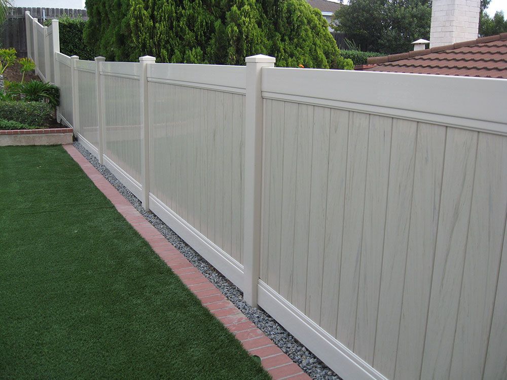 White vinyl fence along a green lawn and brick border in a residential yard.