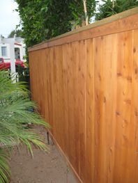 Wooden fence along a narrow path with green plants and a white house in the background