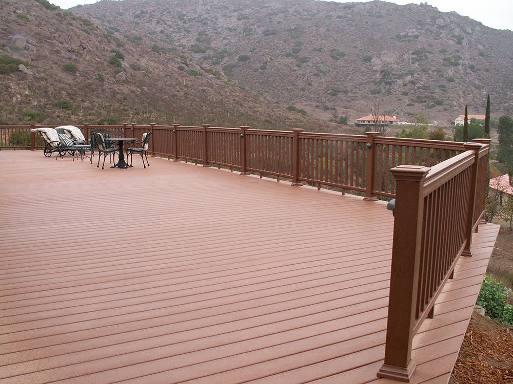 Wooden deck with brown railing overlooking rocky mountains, with lounge chairs in the distance.