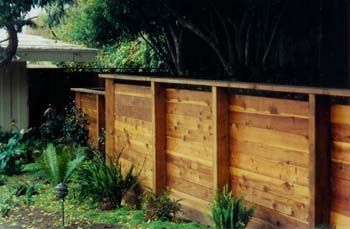 Wooden fence along a lush garden with trees and tropical plants