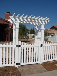 White picket gate and pergola arbor in a front yard under a clear blue sky