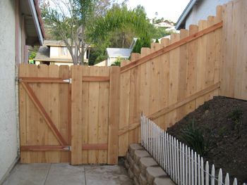 Wooden fence and gate beside a sloped yard with retaining wall and white picket edging