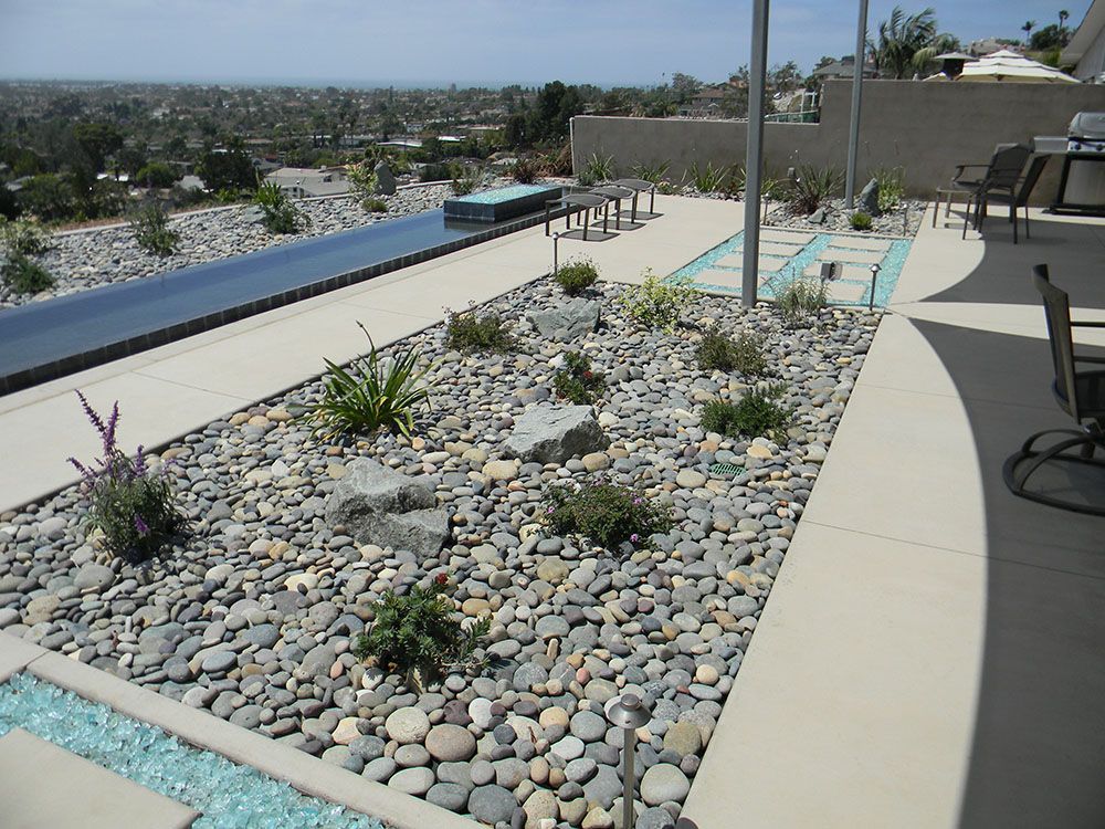 Rooftop patio with pebbled succulent garden, infinity pool, and lounge chairs overlooking a city view