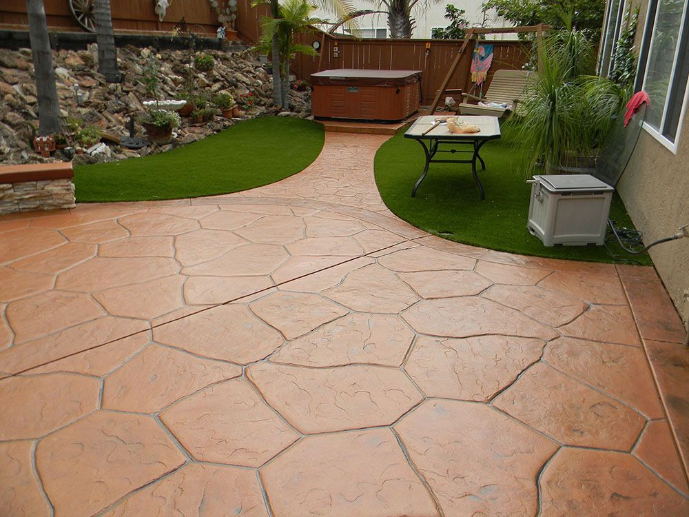 Backyard patio with stamped concrete, artificial grass, a hot tub, and a picnic table