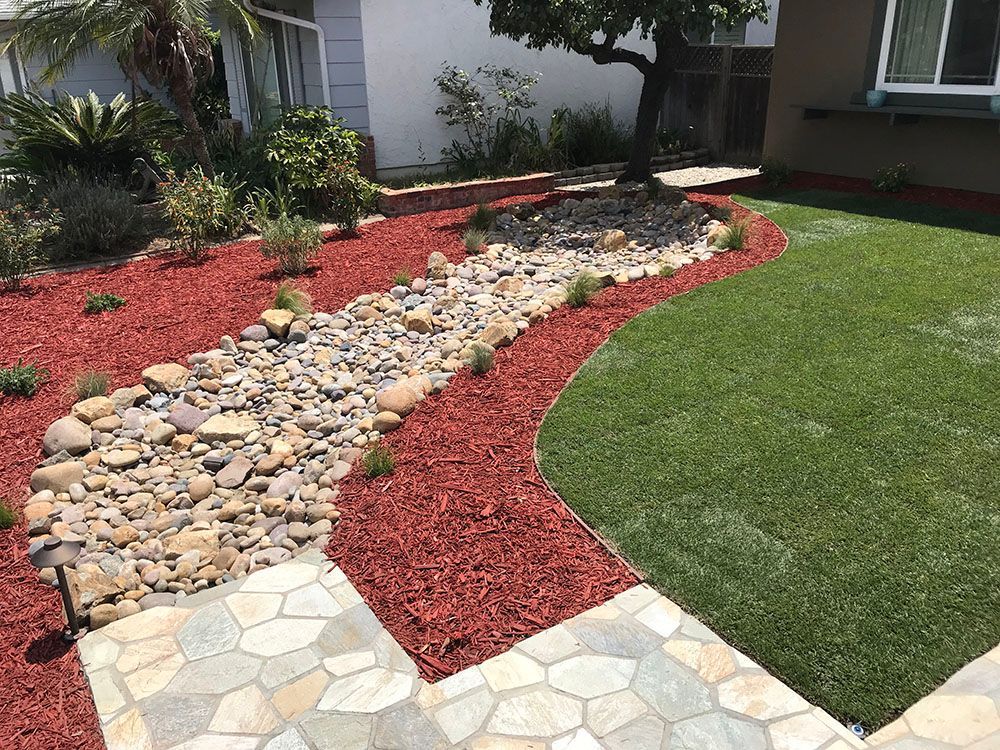 Front yard landscaping with red mulch, decorative rocks, and a curved stone walkway beside green lawn