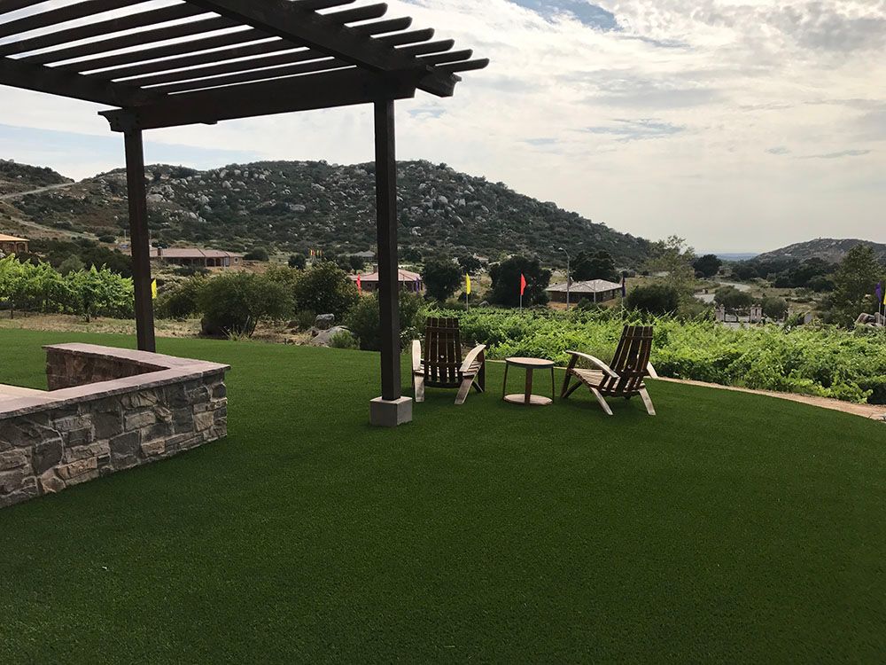 Patio with green lawn, lounge chairs, pergola, and a scenic hillside view under a cloudy sky