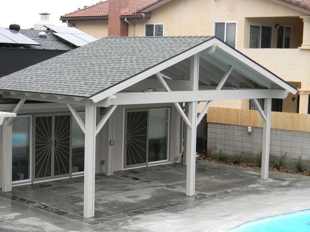 Covered driveway carport with gray roof and white posts beside a house