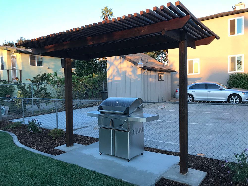 Covered outdoor grill area with a stainless steel barbecue in a paved courtyard beside apartment buildings