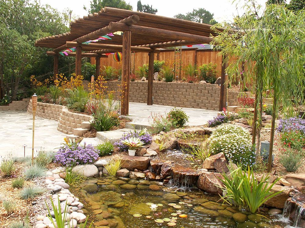 Garden pond with rocks, flowers, and a wooden pergola over a stone patio