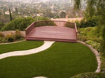 Backyard patio with curved lawn, stone path, and wooden deck overlooking a hazy city view