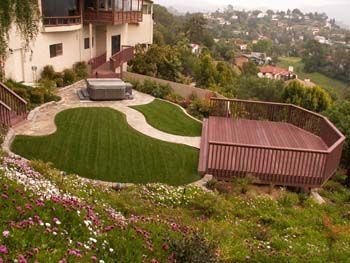 Terraced hillside backyard with a green lawn, patio seating, and valley views beyond the house