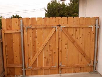 Wooden double gate with diagonal braces and a metal latch in a fenced yard