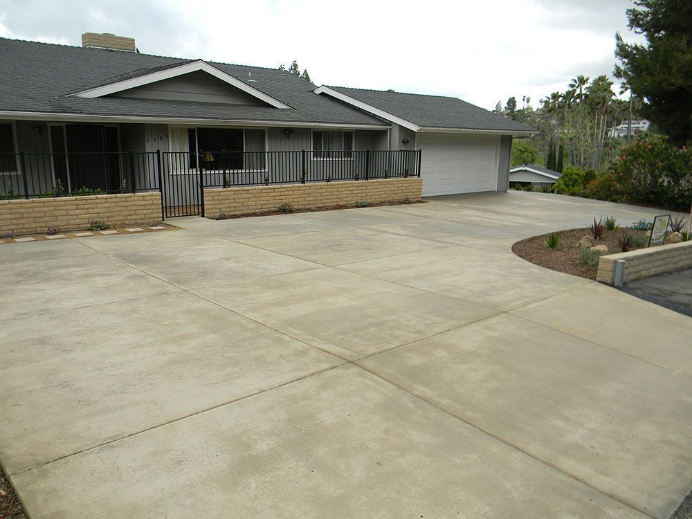 Large concrete driveway leading to a single-story house with a garage and low front fence
