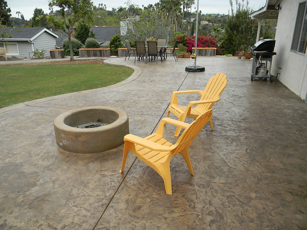 Patio with two yellow lounge chairs beside a round fire pit on a stone walkway