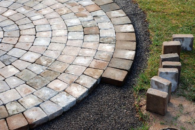 Circular patio construction with pavers. Gray and brown bricks are being laid in concentric circles.