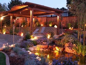 Landscape garden with lit pergola, stone steps, and a small pond at dusk