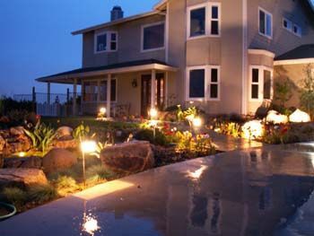 Two-story house with lit garden and pool at dusk