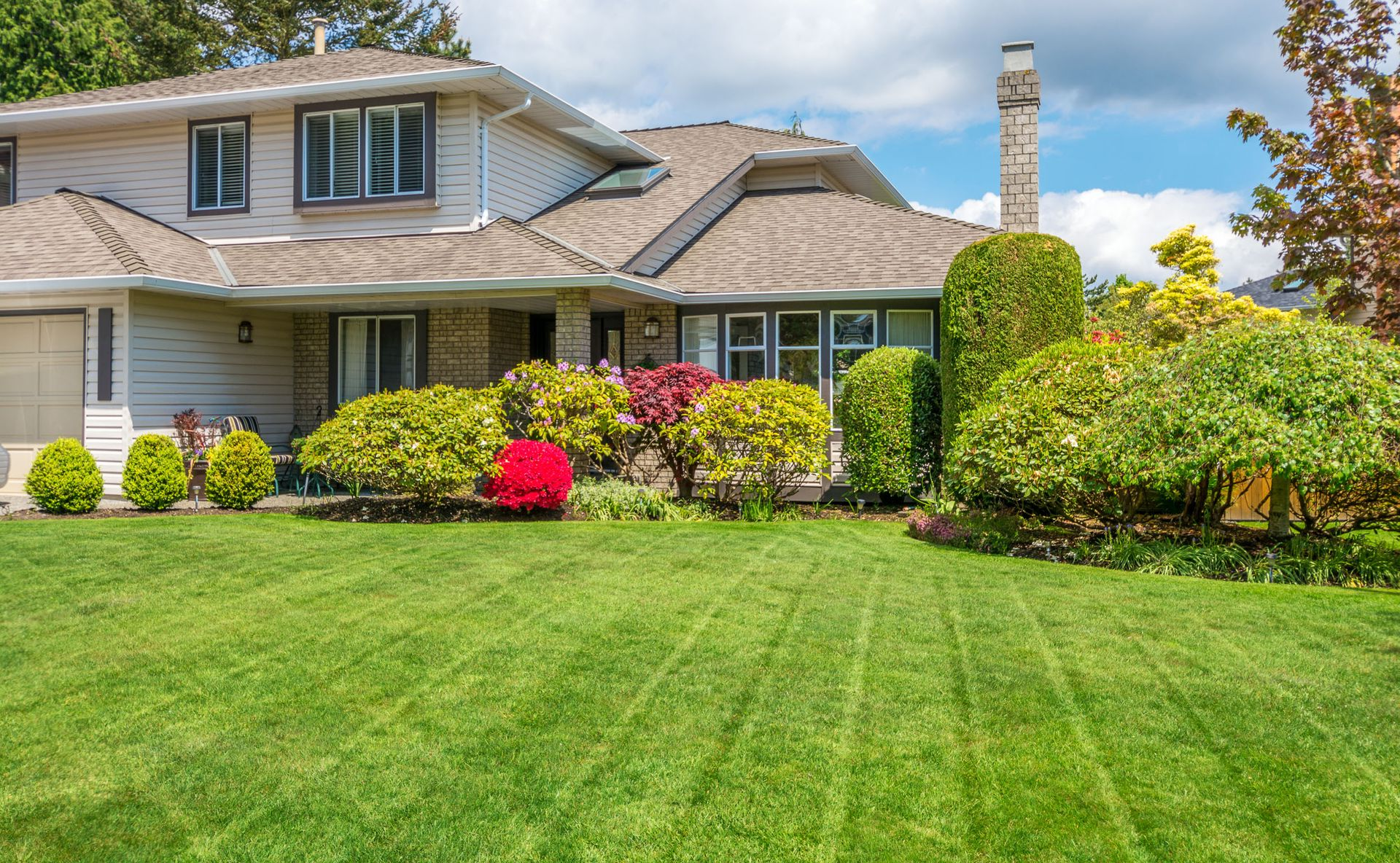 House with green lawn, landscaping, and blue sky.