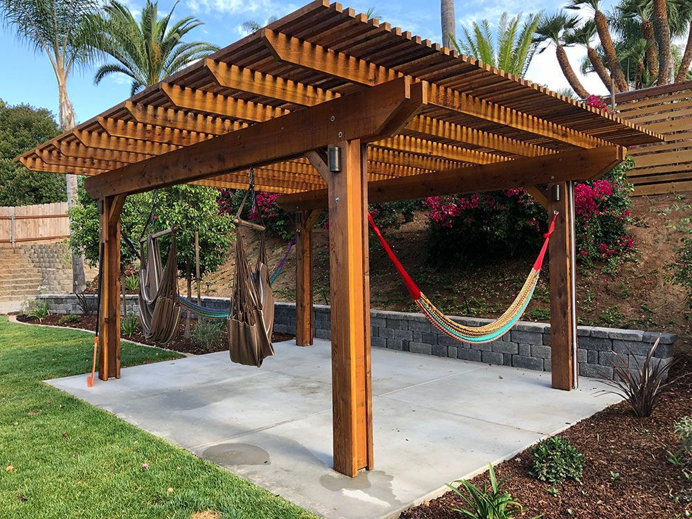 Wooden pergola with a hammock over a concrete patio in a landscaped backyard