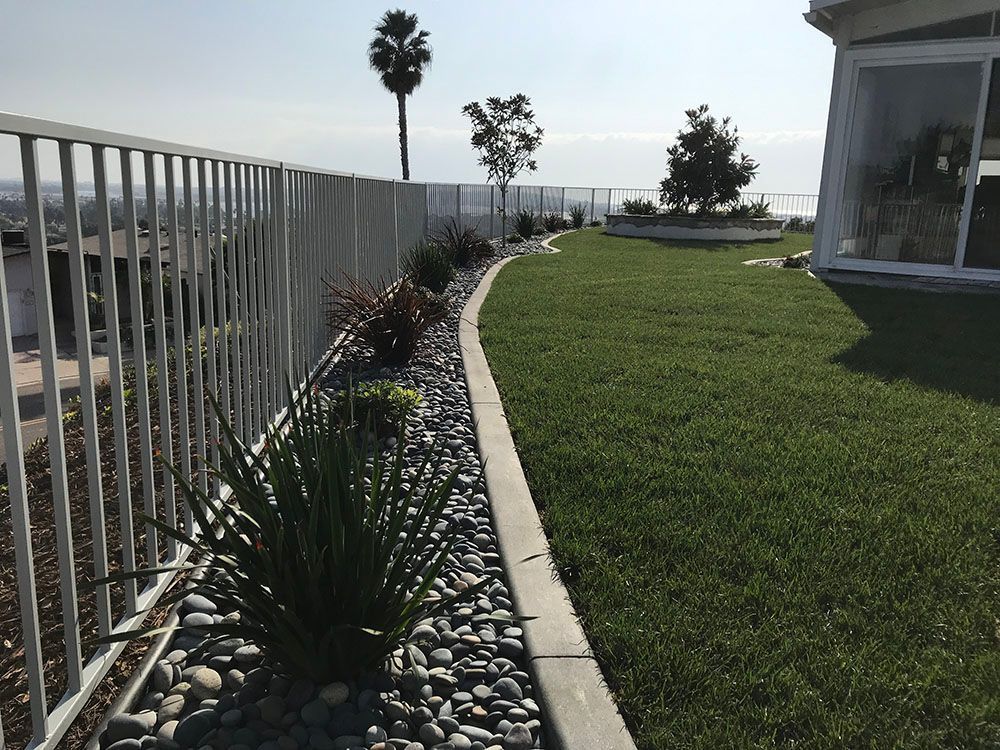 Coastal garden path with green lawn, stone border, and ocean view beside a white fence