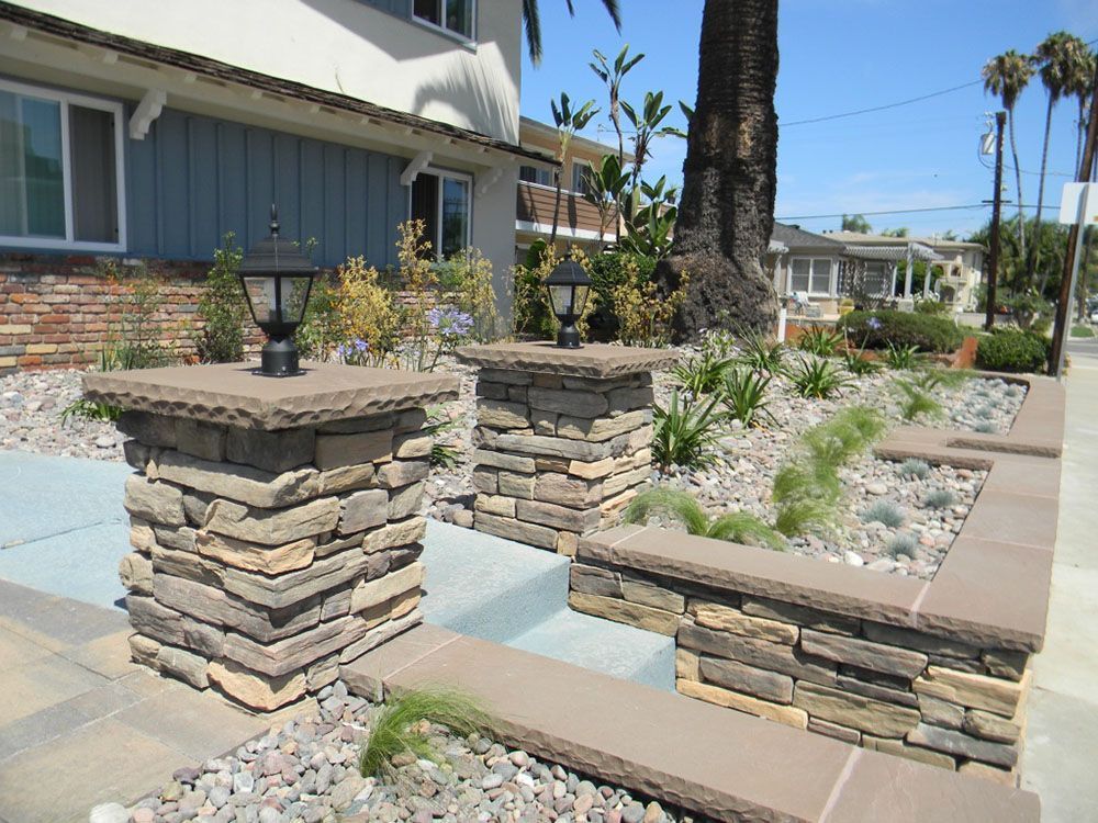 Front walkway with stacked-stone pillars, low wall, and landscaped garden beside a house