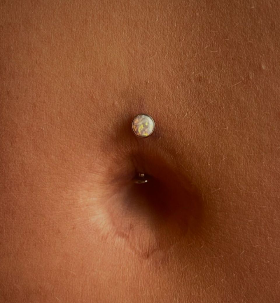 A close-up of a woman's belly with a belly button ring.