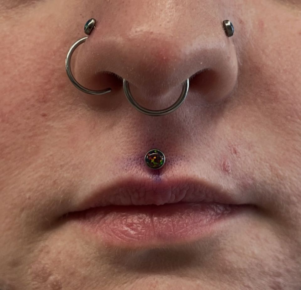 A close-up of a person's face with a nose ring and lip piercing.
