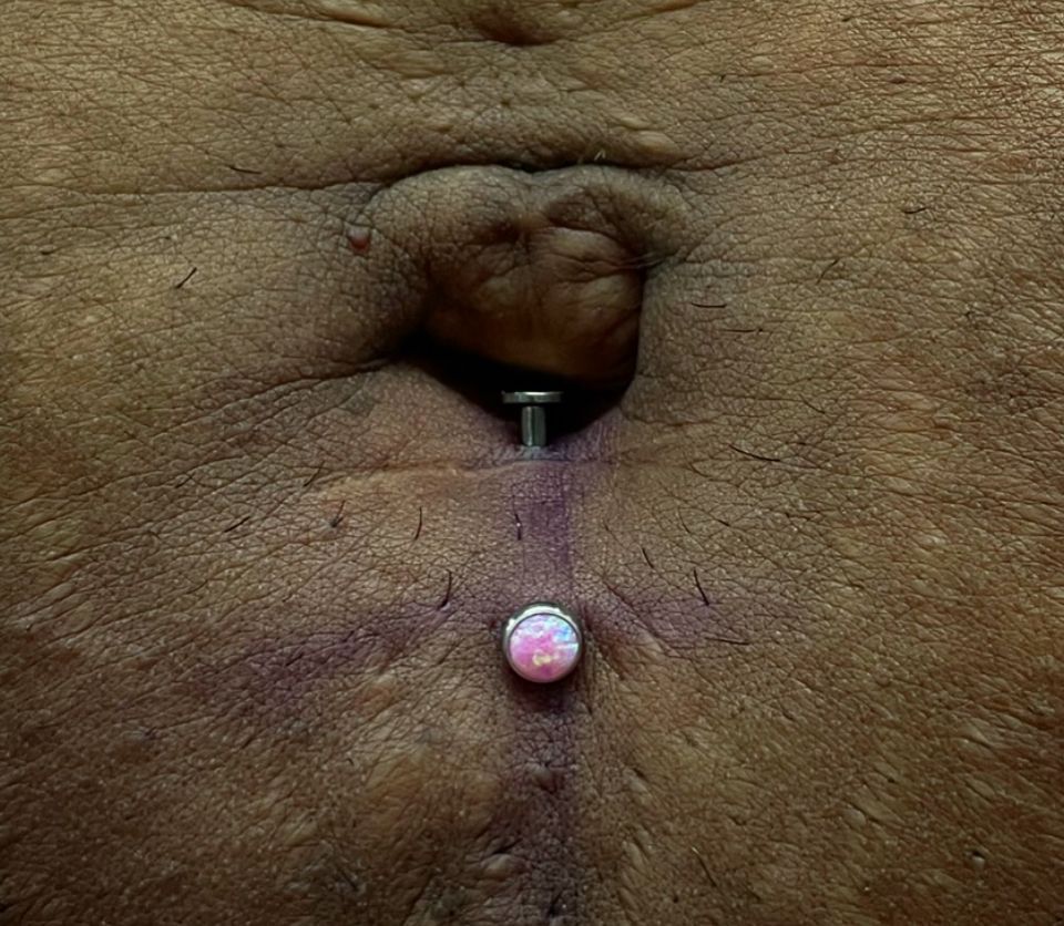 A close-up of a person's belly with a belly piercing.