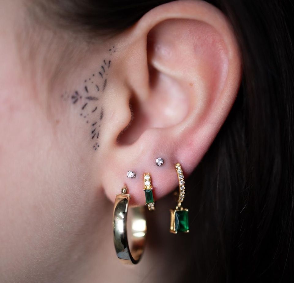 A close-up of a woman's ear with earrings and a tattoo