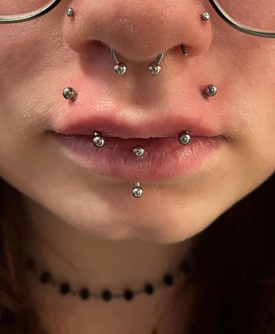 A close-up of a woman's face with piercings and glasses.