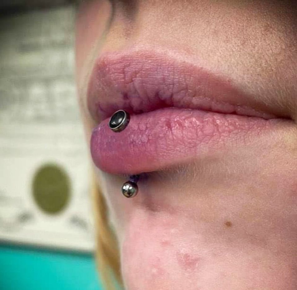 A close-up of a woman's lips with a lip piercing.