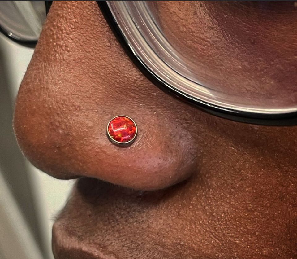 A close-up of a person's nose with a red nose ring