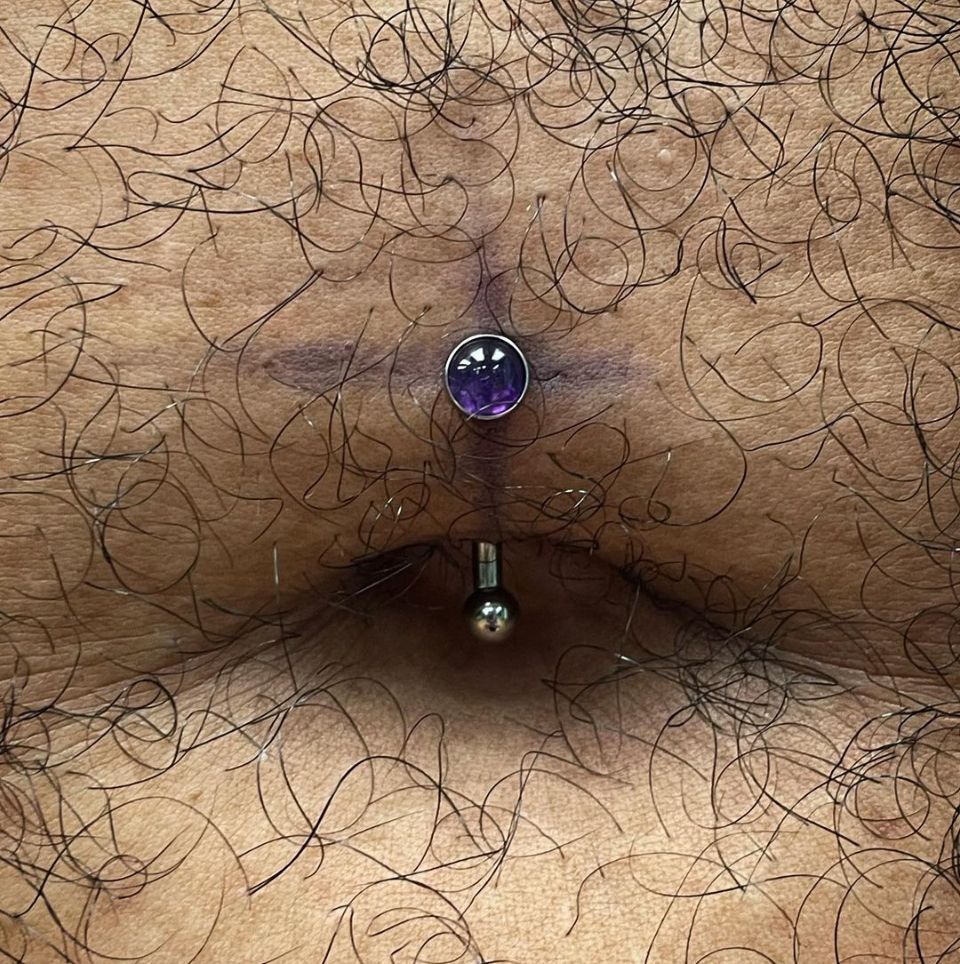 A close-up image of a person's belly with a belly piercing.