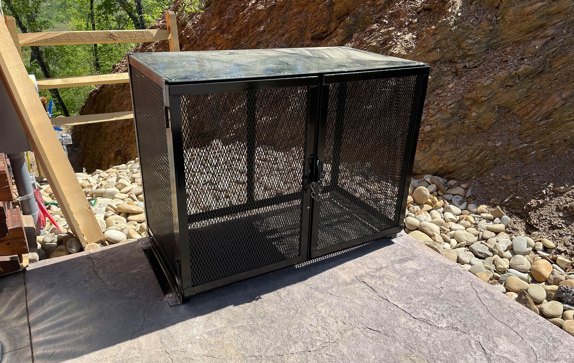 a metal cage is sitting on a patio next to a rocky hillside .