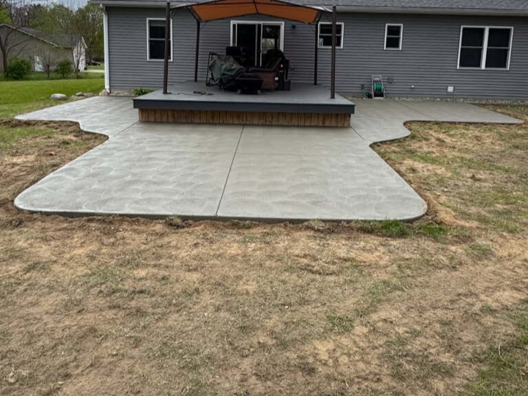Backyard patio with covered deck and concrete walkway leading to a gray house under cloudy skies