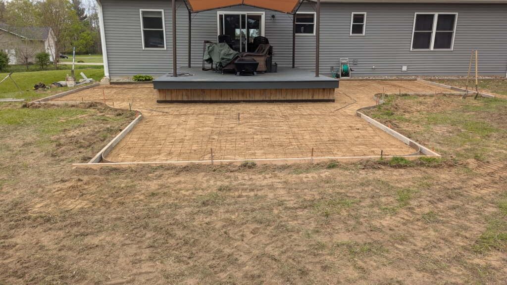 Backyard with a raised wooden deck, empty framed patio area, and gray house exterior