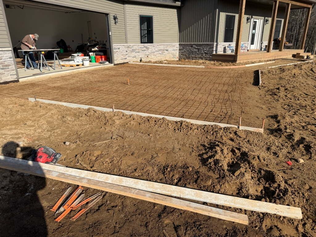 Backyard patio construction with concrete forms, gravel, and workers near a house