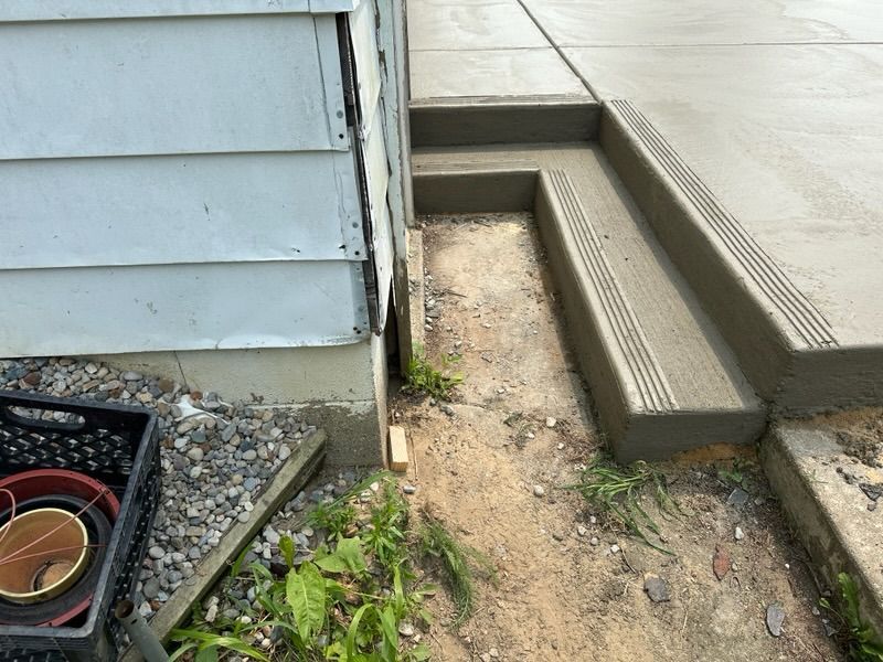 Side of a house with a concrete walkway, narrow drainage channel, and a basement window well.