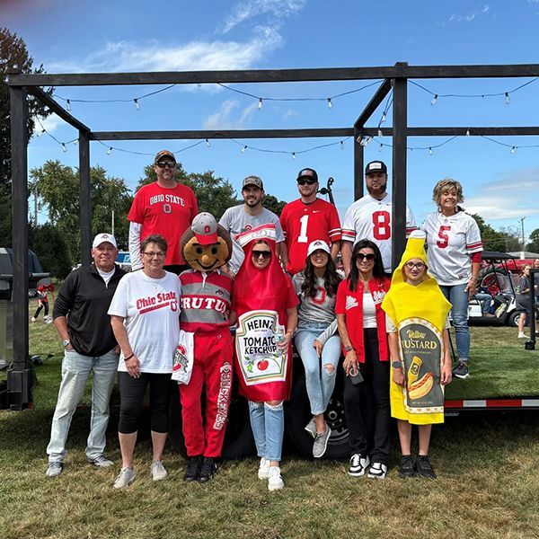 Group in Nebraska Cornhuskers gear posing on a float at an outdoor event, with a string-light frame backdrop